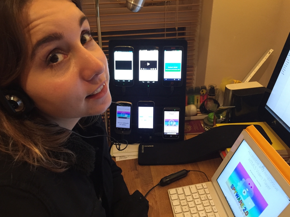 Laura sitting in front of 6 phones, a tablet and a desktop computer